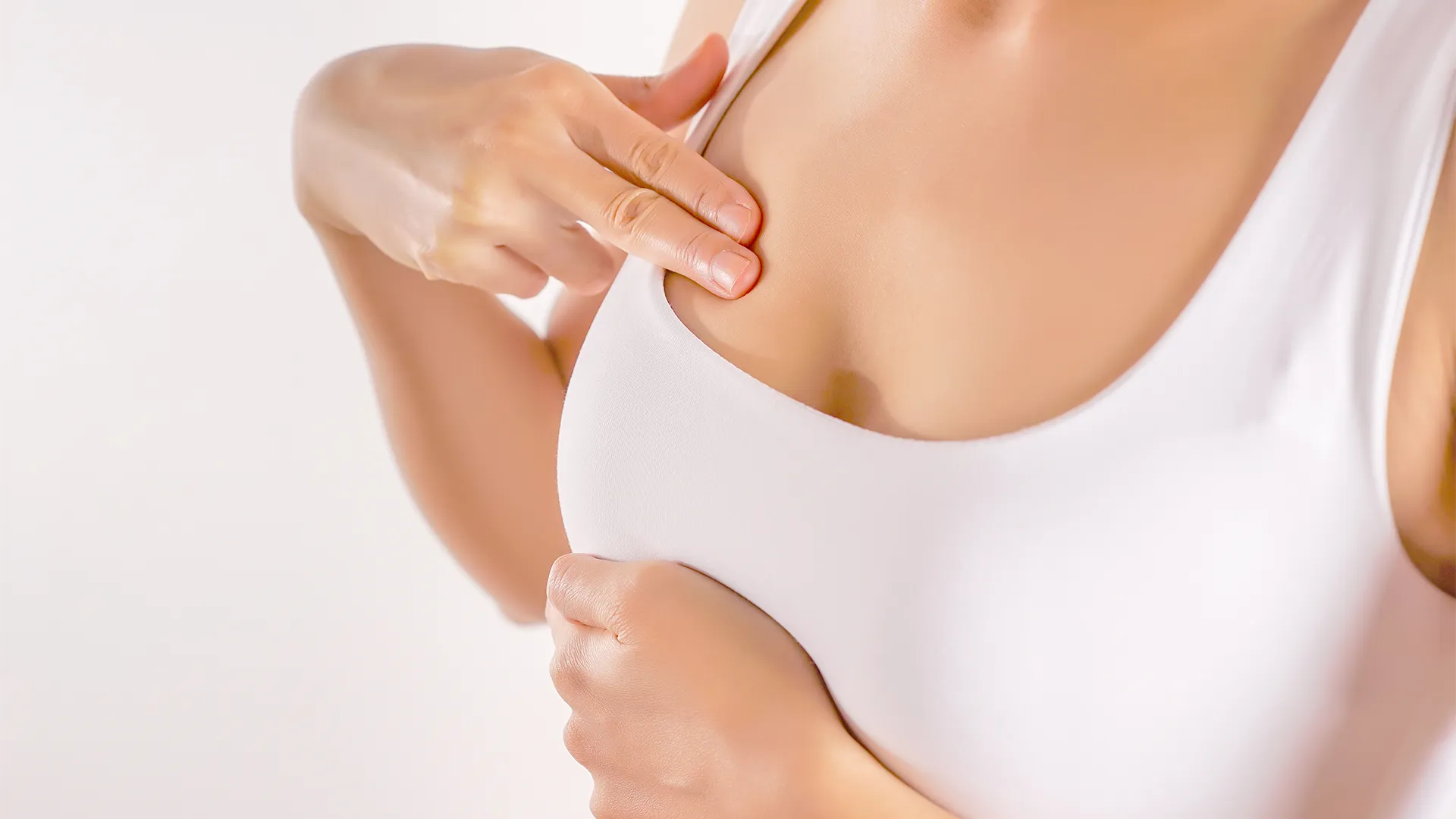 Woman wearing a white tank top performing a breast-self exam